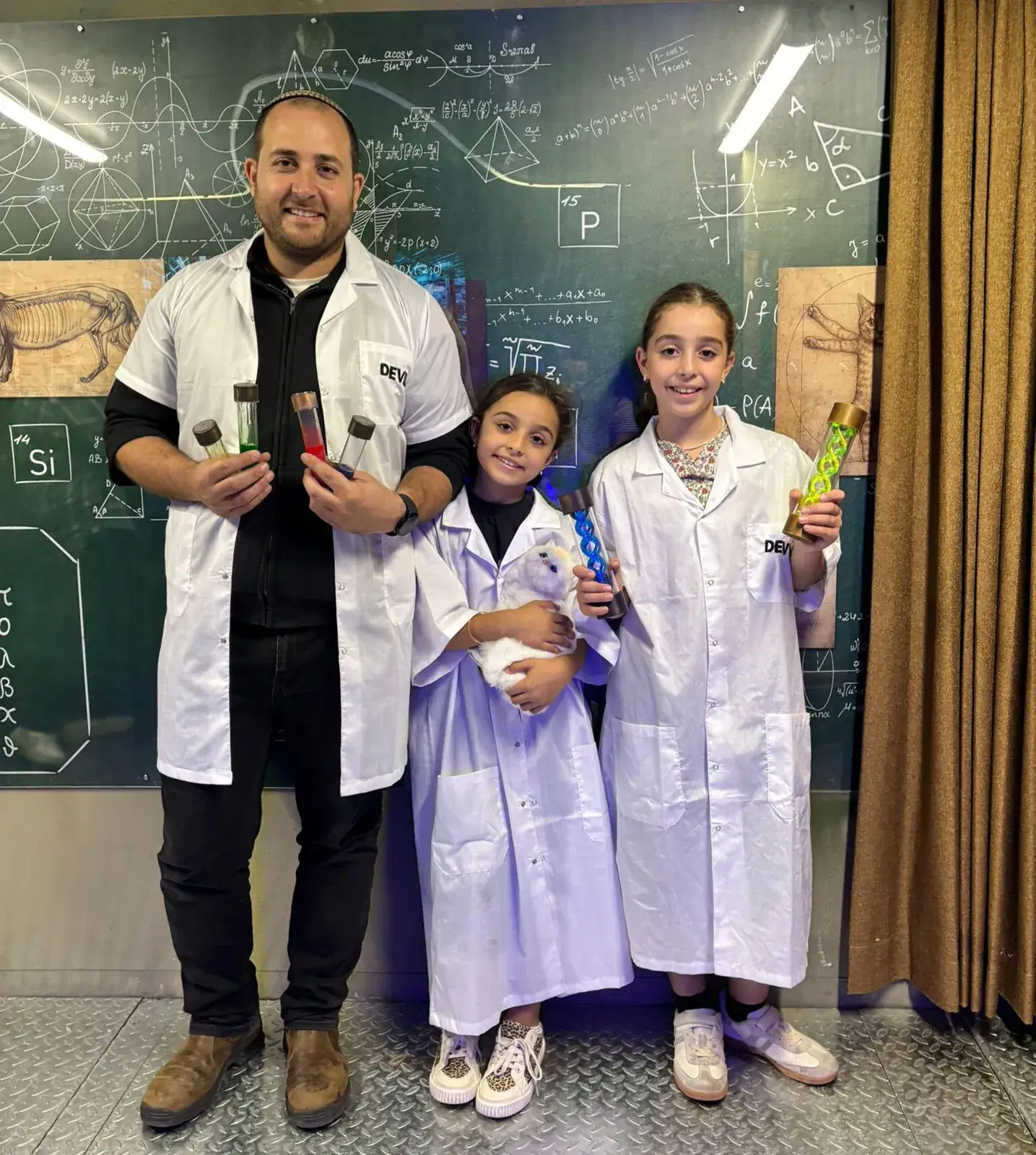 שחקנים בחלוקי מעבדה במעבדה של פרופסור דה-ויל